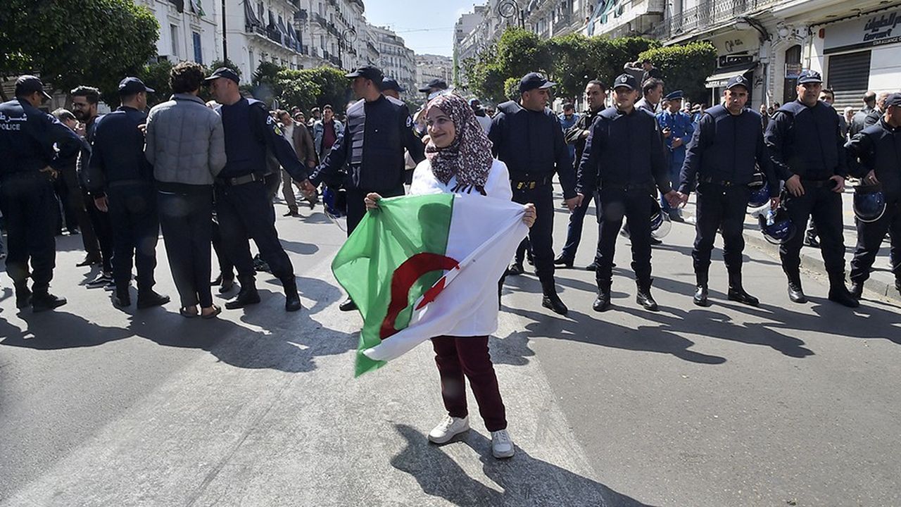 Une enseignante brandit le drapeau algérien devant un cordon de policiers.