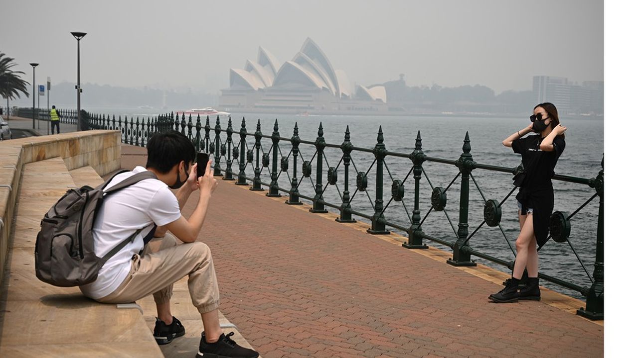 Des touristes masqués se prennent en photo devant l'Opéra de Sidney en décembre dernier dans une atmosphère viciée par la fumée des incendies. 