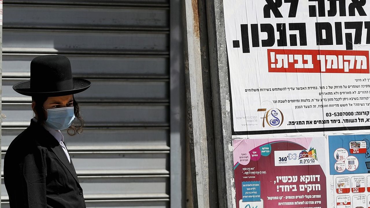 Un Juif ultra-orthodoxe portant un masque passe devant une publicité qui indique en hébreu « si vous lisez ceci c'est que vous n'êtes pas au bon endroit, votre place est à la maison ».