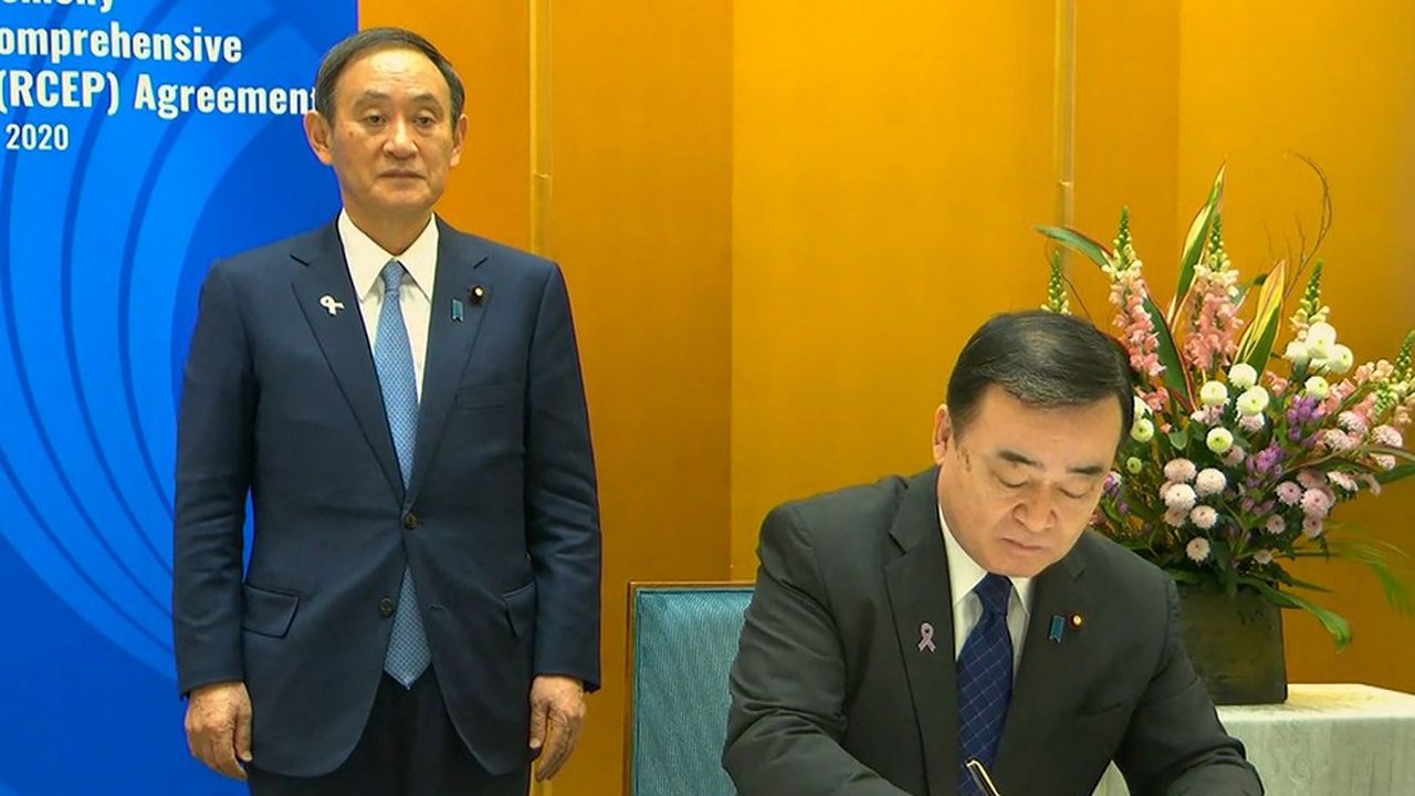 Le Premier ministre du Japon Yoshihide Suga (debout) et son ministre de l'Economie, Hiroshi Kajiyama, à la signature du Partenariat régional économique global.