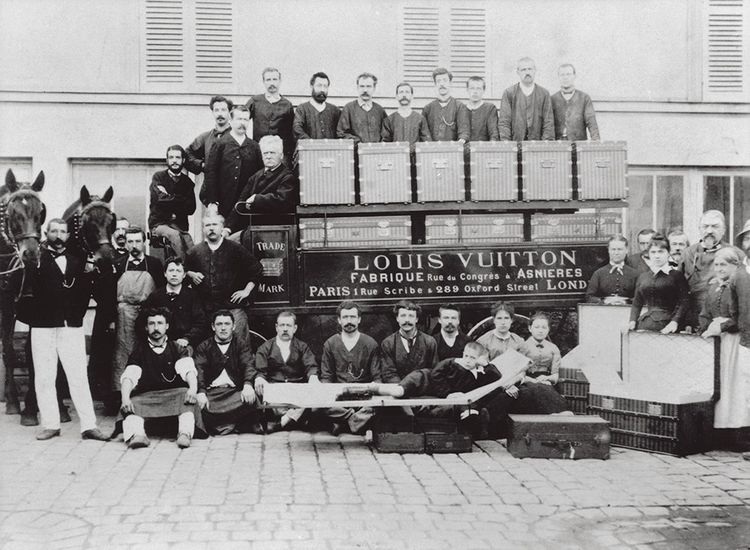 Dans la cour des atelier d'Asnières vers 1888. Louis Vuitton est assis à la place du conducteur, son fils Georges, debout à sa droite. Son petit-fils Gaston-Louis est couché devant sur une malle-lit. À cette époque, la maison emploie une trentaine de personnes.