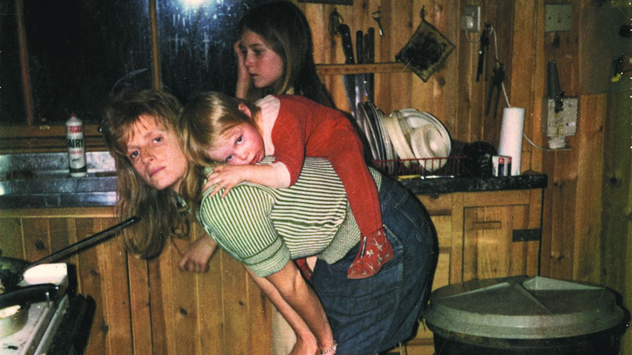 Linda McCartney dans sa cuisine en Ecosse, au milieu des années 1970, avec ses filles Heather (debout) et Stella (sur son dos).