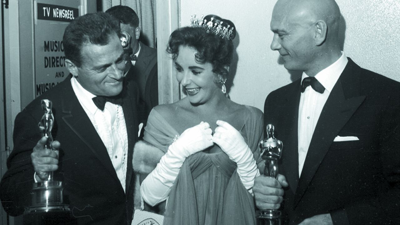 Elizabeth Taylor entourée de son mari, le producteur Mike Todd, et Yul Bryner, le père de Victoria, lors de la cérémonie des oscars de 1957.