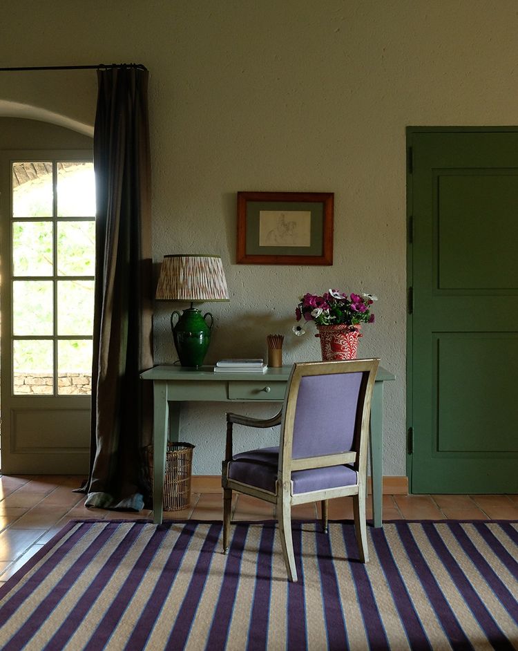Dans une chambre d'amis, on reconnaît sur un simple bureau en bois peint la lampe «Pedro» et le seau à glace «Oiseau» de Casa Lopez. Le fauteuil Directoire est tapissé d'un chevron de lin violet pour donner une touche contemporain. Au sol, le tapis «Rayures Club».