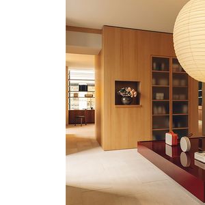 Le bardage en bois sur le mur bibliothèque et le meuble présentoir rouge bordeaux confèrent à l'espace, teinté de beige, de la douceur.
