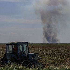 Un agriculteur travaille flegmatiquement son champs en Ukraine alors que les duels d'artillerie se déroulent au loin.