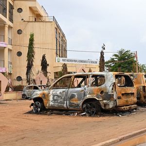 Un vendeur de rue passe devant des voitures incendiées à proximité du siège du parti pour la démocratie et le socialisme, à Niamey, du président renversé Mohamad Bazoum.