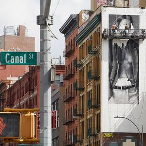 Deux peintres de Colossal Media peignent une publicité pour la marque de prêt-à-porter COS sur un mur d'immeuble, à New York, en novembre 2023.