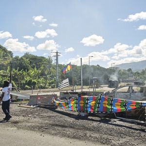 Des personnes tiennent un barrage routier, avec des drapeaux kanaks, contrôlant l'accès à un quartier de Nouméa, le 24 mai 2024.